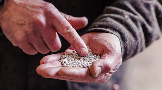vinger van man wijst naar kunstmest in hand