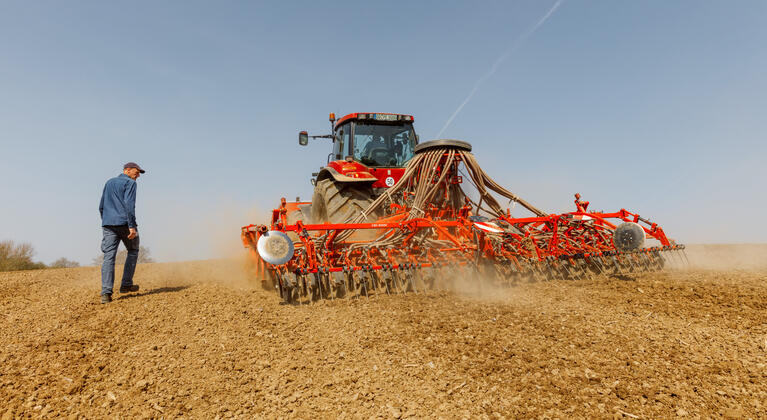 Boer loopt naast trekker met zaaimachine