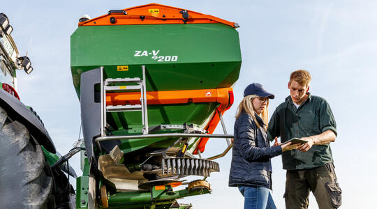 Man en vrouw staan naast kunstmeststrooier en kijke naar tablet
