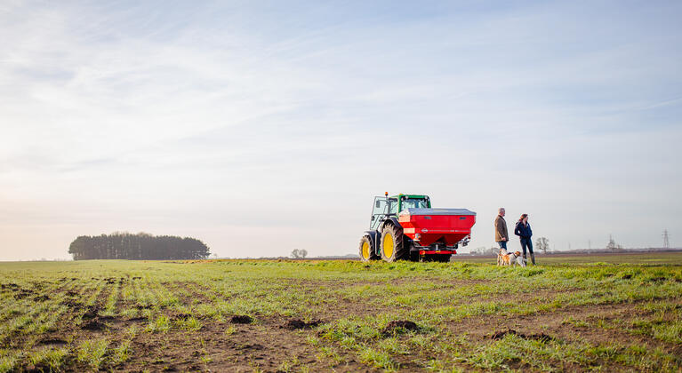 Man, vrouw en hond met John Deere en kunstmeststrooier op het land