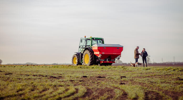 man en vrouw bij kunstmeststrooier in het veld