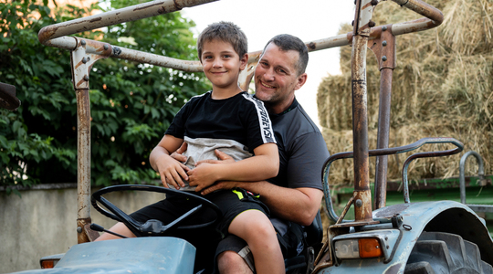 Boy sitting on father's lap while on tractor